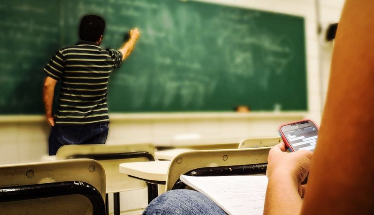 Aula escolar en Santa Fe con estudiantes y teléfonos celulares sobre los bancos